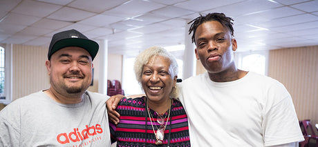 Three people standing with arms around each other in a room.