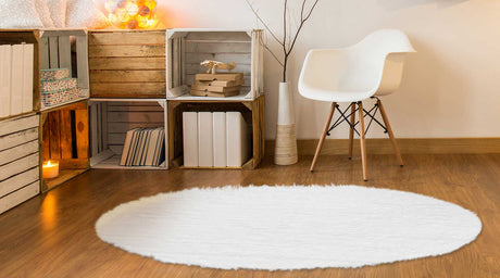 A room with hard wood floors, a My Magic Carpet white shag rug, console block shelving, a vintage plastic and wood chair next to a tree.