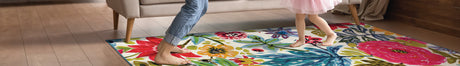 Mom and daughter dancing on a colorful floral My Magic Carpet rug in a living room with windows