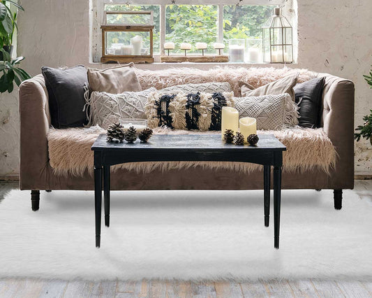 Living room couch by a window with a shag rug under a coffee table with candles.