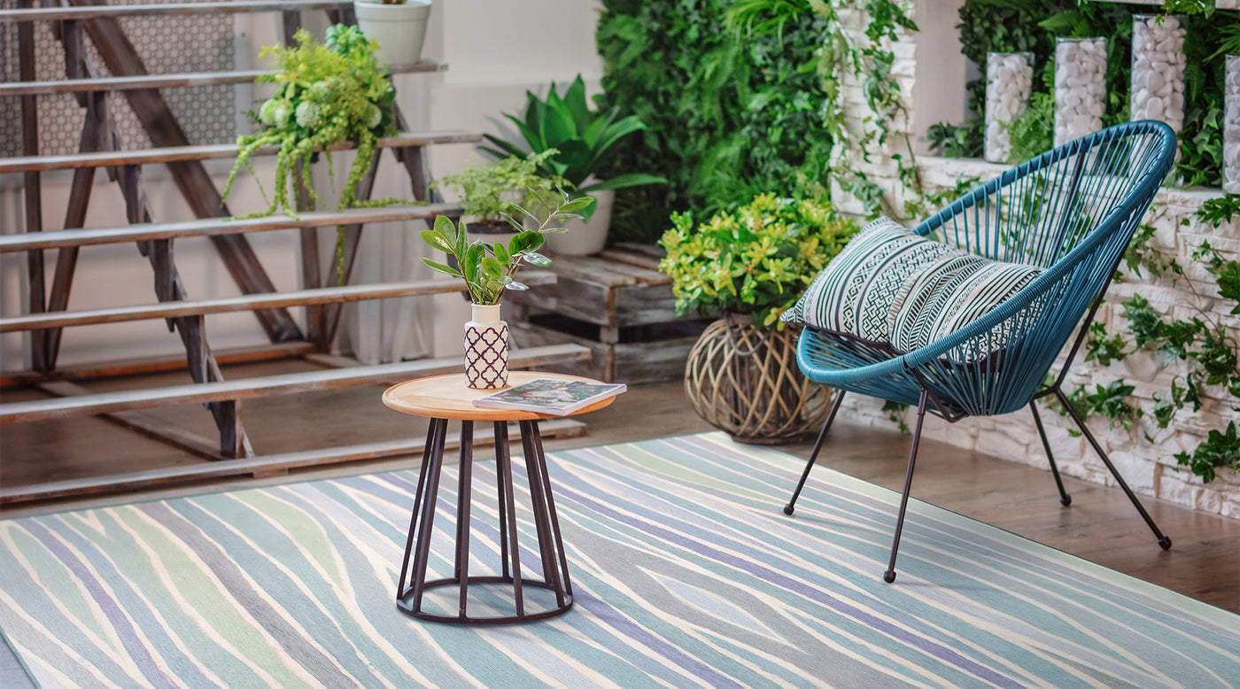 Ocean waves carpet in blue on a patio with an Acapulco chair, plants and small coffee table.