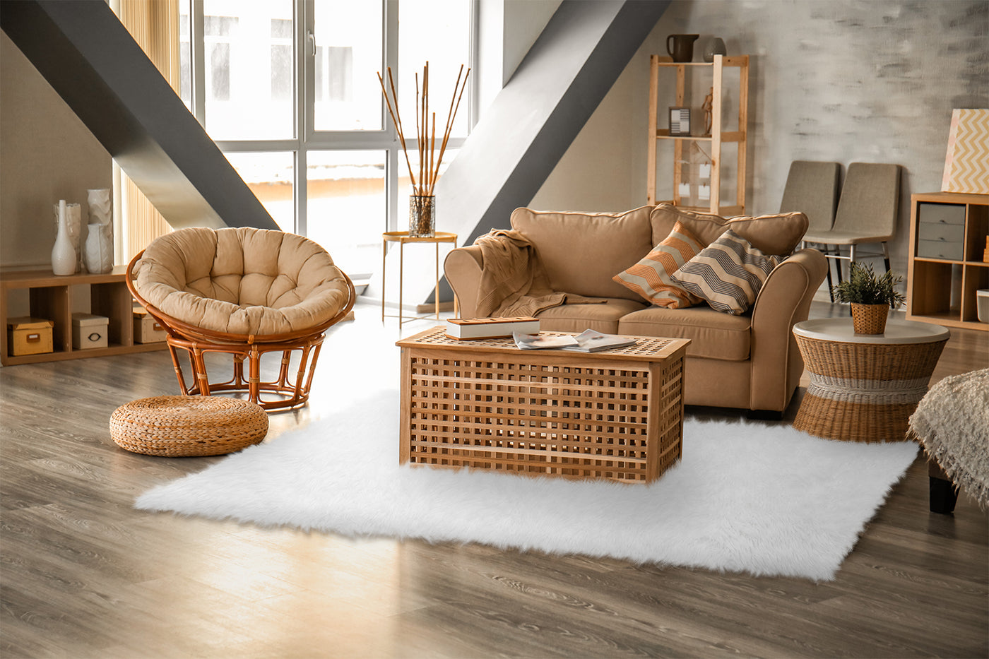cream colored shag rug with wicker trunk coffee table, wicker side table, hard wood floors, a tan colored couch with throw pillows three wood book cases placed around the room and a papasan chair. 